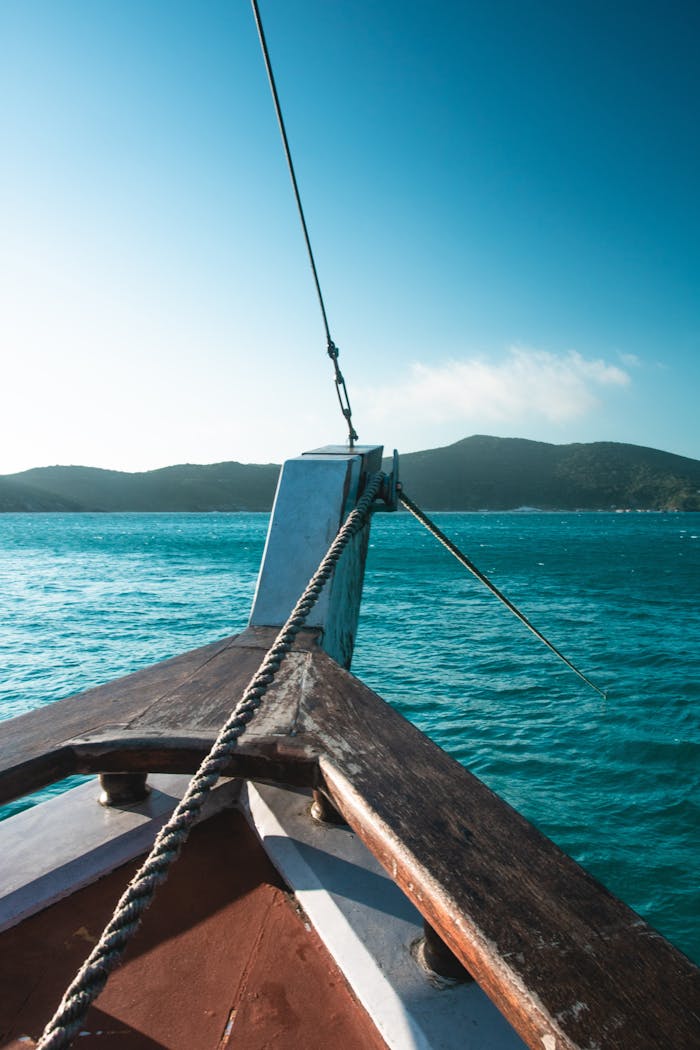 A serene view from a wooden sailboat sailing in the calm summer ocean under a clear blue sky.