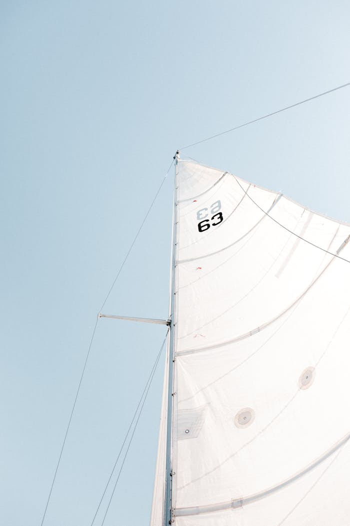 Minimalist view of a sailboat's mast and sails under a clear blue sky, creating a sense of adventure and freedom.