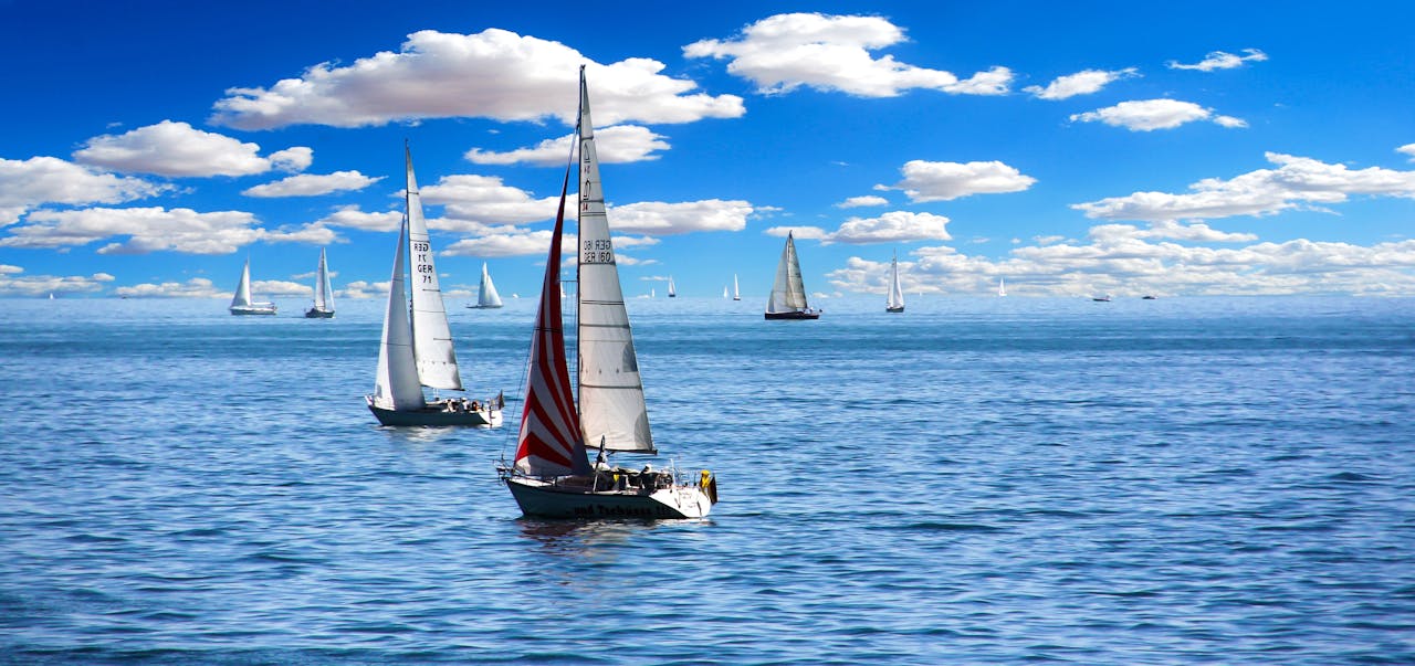 Vibrant sailboats sailing under a clear blue sky with fluffy clouds.